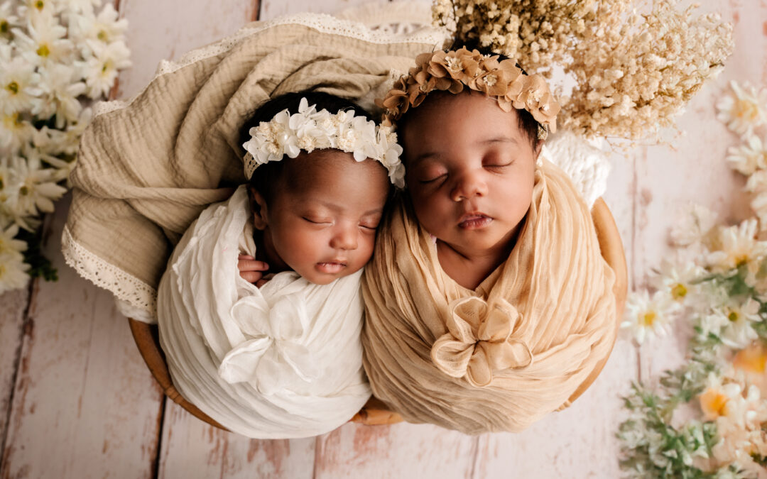 Twee pasgeboren tweelingbaby’s slapend samen, gekleed in witte outfits met bloemenhoofdbanden, gefotografeerd in Almere.