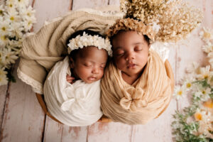 Twee pasgeboren tweelingbaby’s slapend samen, gekleed in witte outfits met bloemenhoofdbanden, gefotografeerd in Almere.