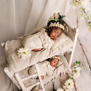 Twee pasgeboren tweelingbaby’s slapend samen, gekleed in witte outfits met bloemenhoofdbanden, gefotografeerd in Almere.