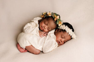 Twee pasgeboren tweelingbaby’s slapend samen, gekleed in witte outfits met bloemenhoofdbanden, gefotografeerd in Almere.