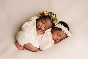 Twee pasgeboren tweelingbaby’s slapend samen, gekleed in witte outfits met bloemenhoofdbanden, gefotografeerd in Almere.