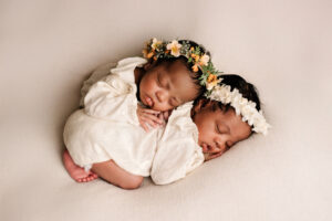 Twee pasgeboren tweelingbaby’s slapend samen, gekleed in witte outfits met bloemenhoofdbanden, gefotografeerd in Almere.
