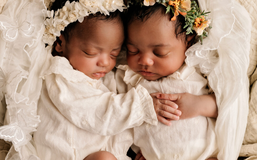Twee pasgeboren tweelingbaby’s slapend samen, gekleed in witte outfits met bloemenhoofdbanden, gefotografeerd in Almere.