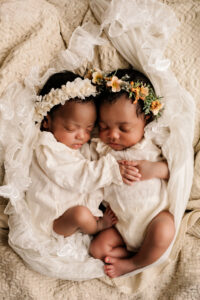 Twee pasgeboren tweelingbaby’s slapend samen, gekleed in witte outfits met bloemenhoofdbanden, gefotografeerd in Almere.