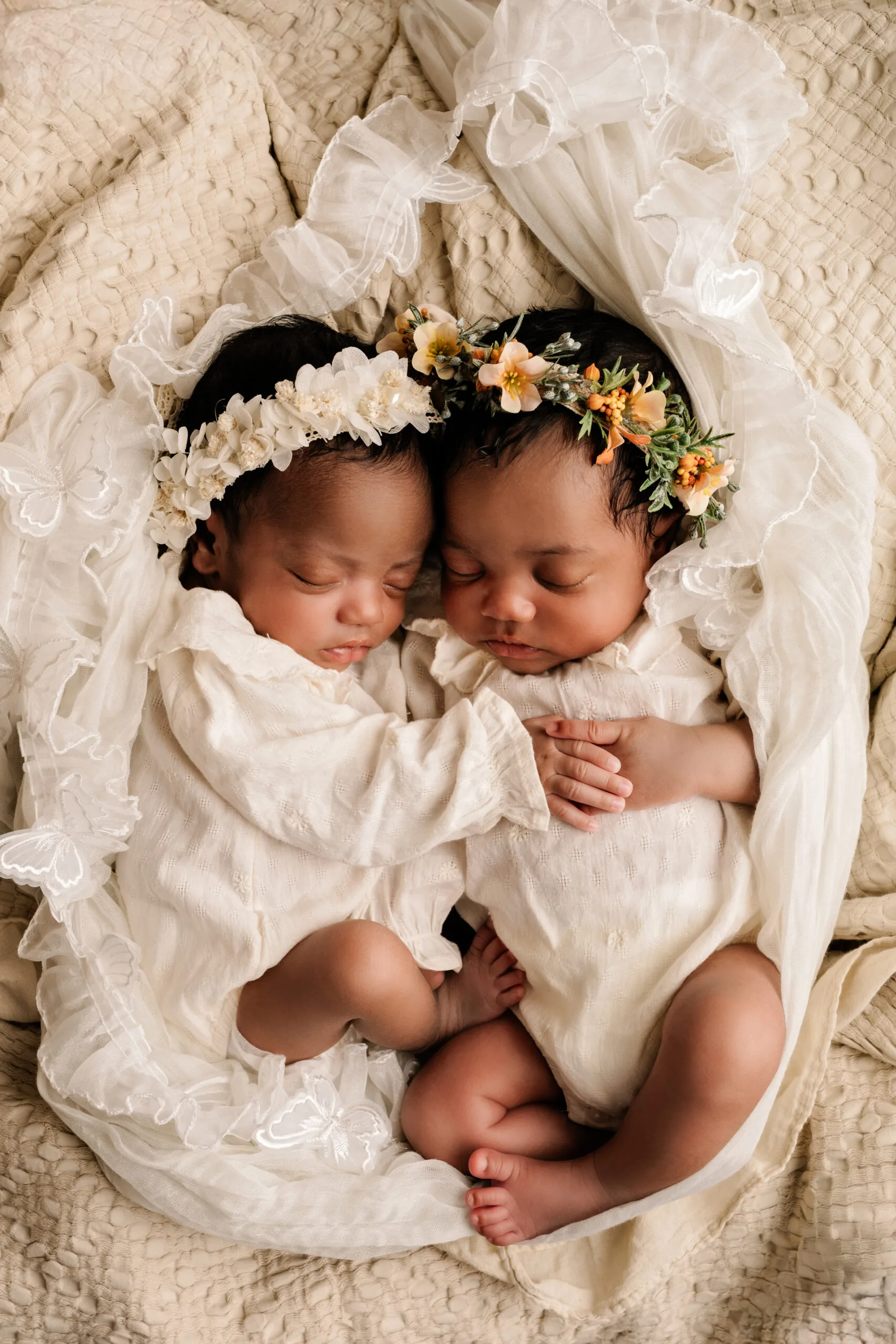 Twee pasgeboren tweelingbaby’s slapend samen, gekleed in witte outfits met bloemenhoofdbanden, gefotografeerd in Almere.