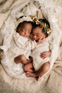 Twee pasgeboren tweelingbaby’s slapend samen, gekleed in witte outfits met bloemenhoofdbanden, gefotografeerd in Almere.
