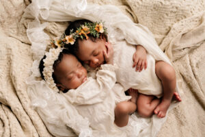 Twee pasgeboren tweelingbaby’s slapend samen, gekleed in witte outfits met bloemenhoofdbanden, gefotografeerd in Almere.