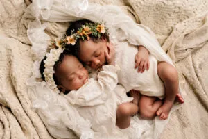 Twee pasgeboren tweelingbaby’s slapend samen, gekleed in witte outfits met bloemenhoofdbanden, gefotografeerd in Almere.