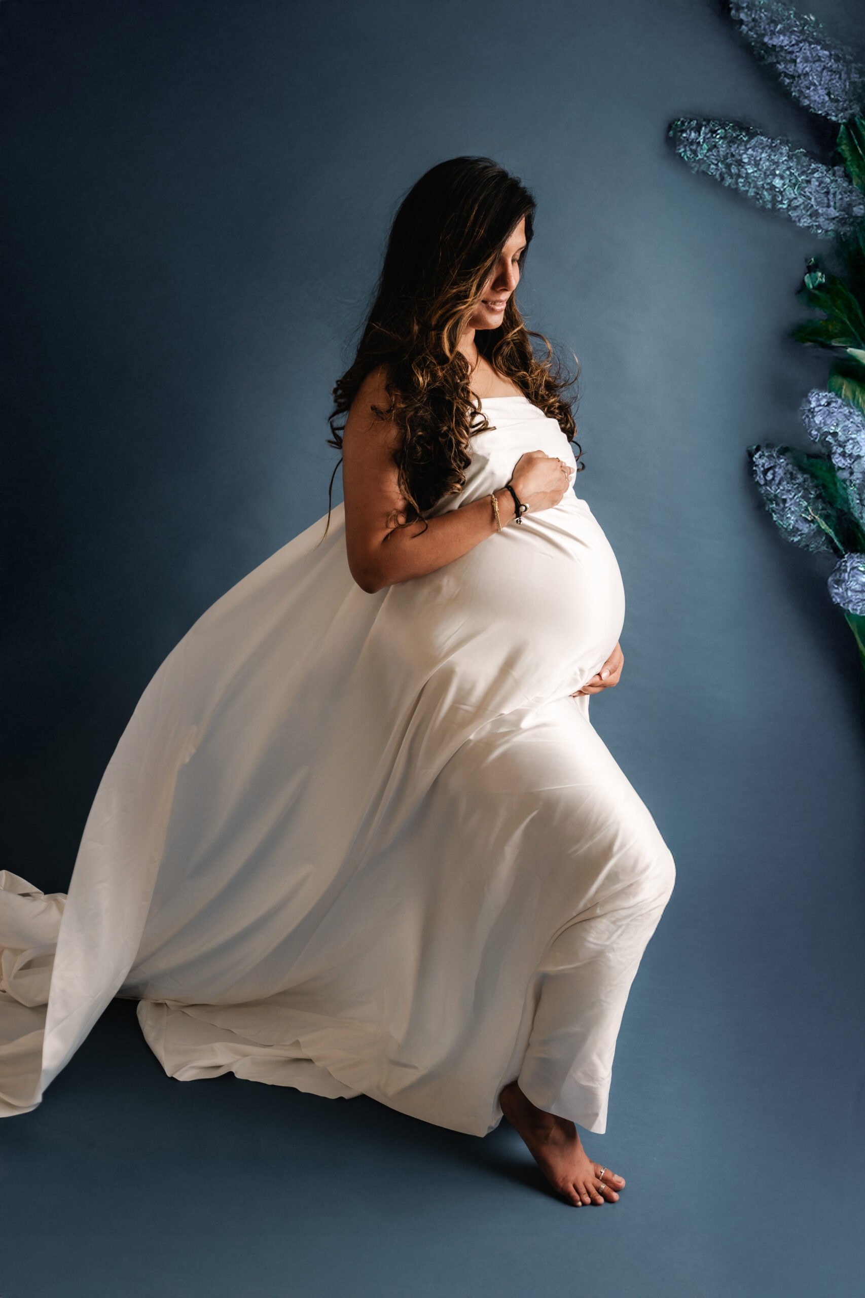 Zwangere vrouw in witte, golvende stof tijdens artistieke zwangerschapsshoot in studio Almere