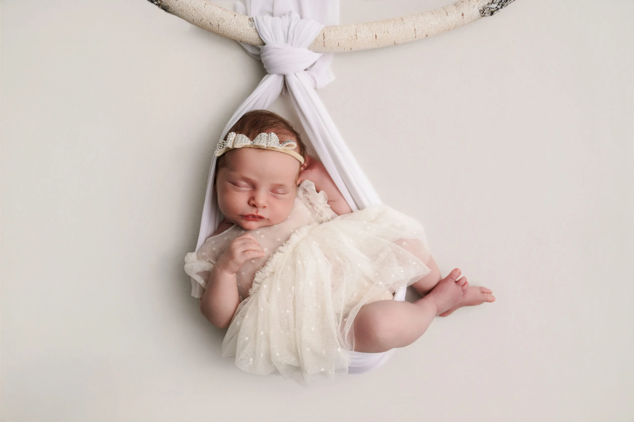 Newborn fotoshoot in Almere – veilige en professionele fotografie Pasgeboren baby in een witte doek hanger, veilig gefotografeerd door gecertificeerde newborn fotograaf in Almere