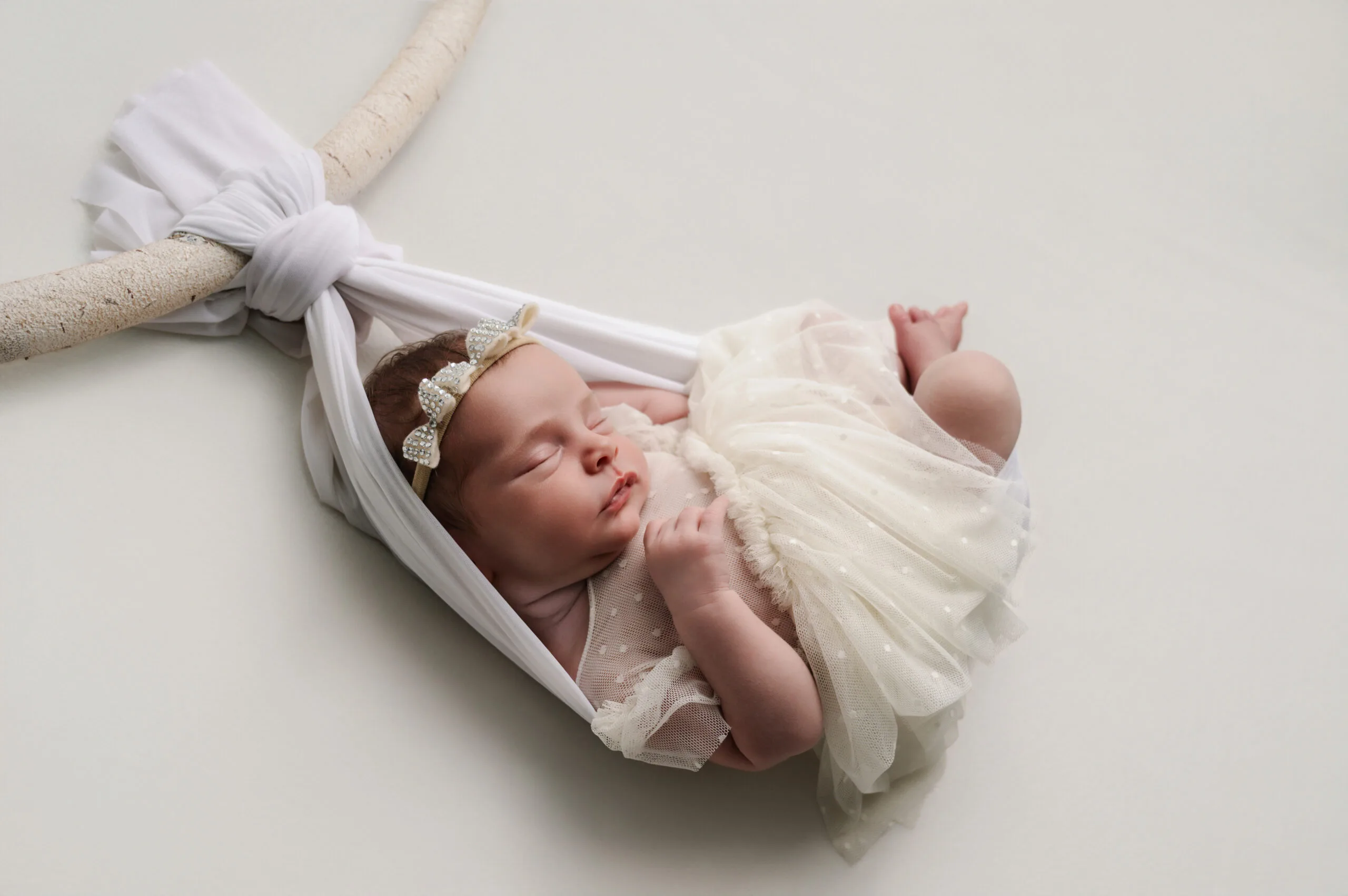 Newborn fotoshoot in Almere – veilige en professionele fotografie Pasgeboren baby in een witte doek hanger, veilig gefotografeerd door gecertificeerde newborn fotograaf in Almere