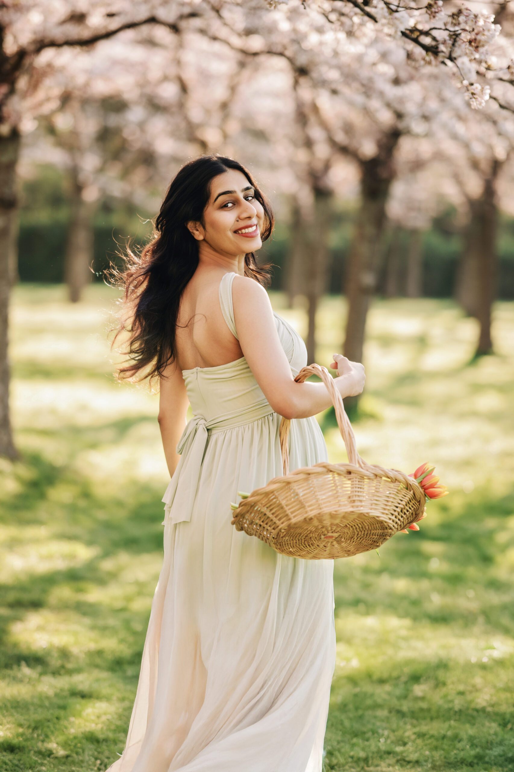 Pregnant woman standing under pink cherry blossom trees during a dreamy spring maternity photoshoot in Amstelveen