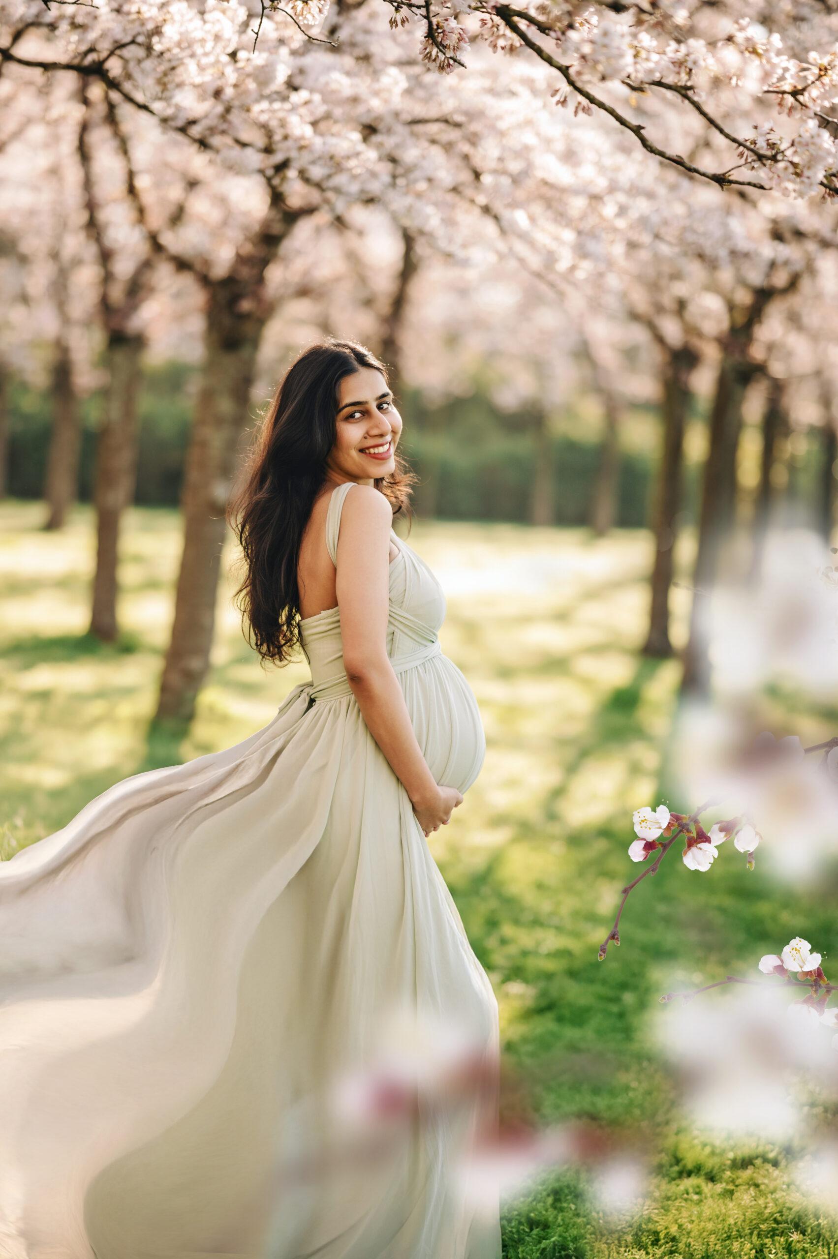Pregnant woman standing under pink cherry blossom trees during a dreamy spring maternity photoshoot in Amstelveen