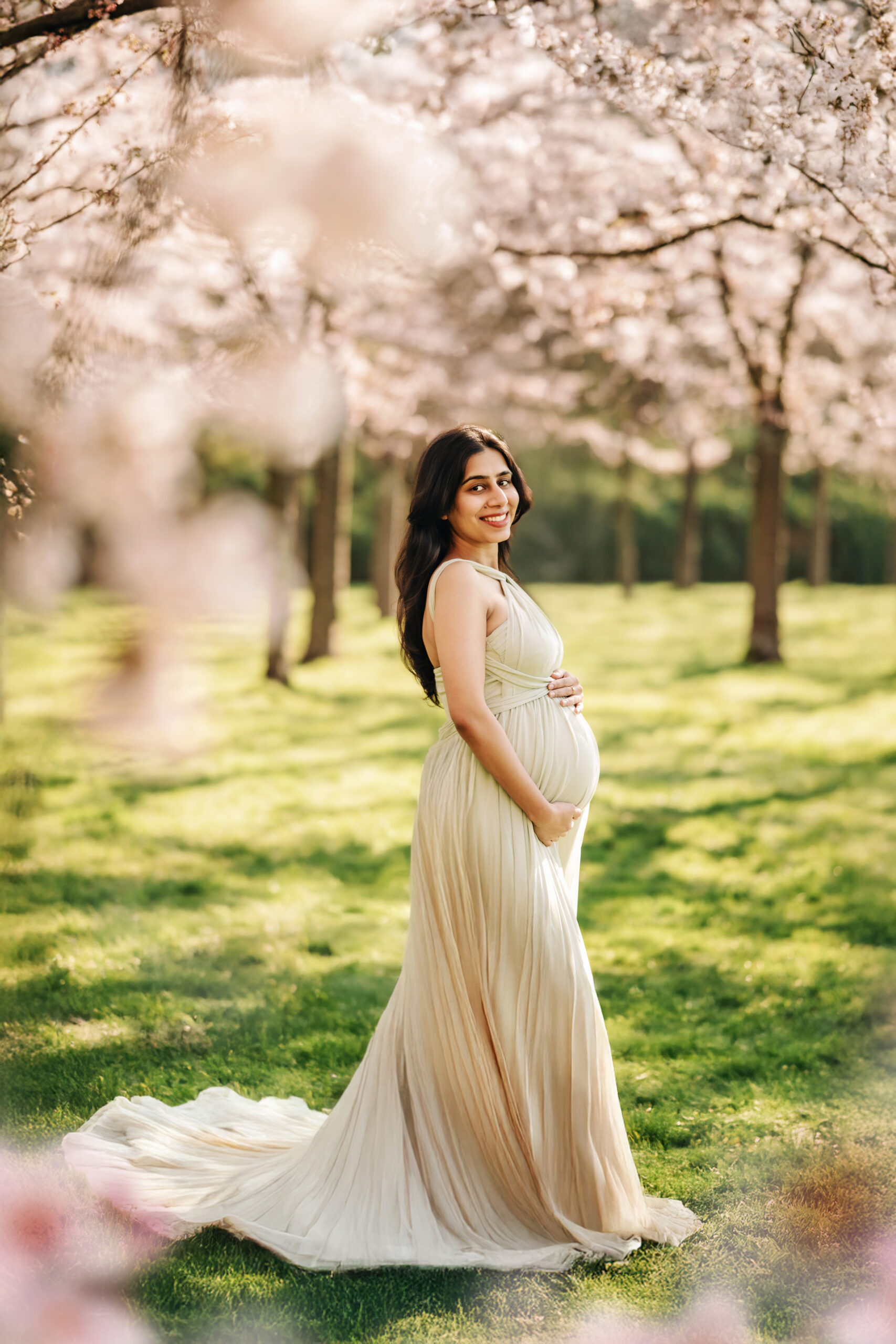 Pregnant woman standing under pink cherry blossom trees during a dreamy spring maternity photoshoot in Amstelveen